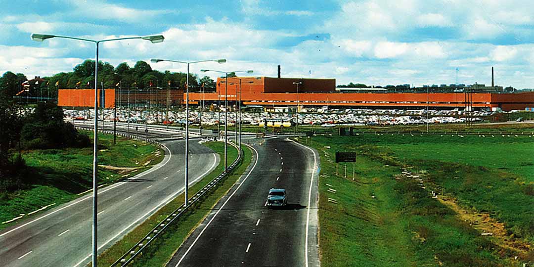 gammalt fotografi från bilvägen och korsningen gamla huddingevägen och åbyvägen. i bakgrunden syns stockholmsmässan med orange fasad