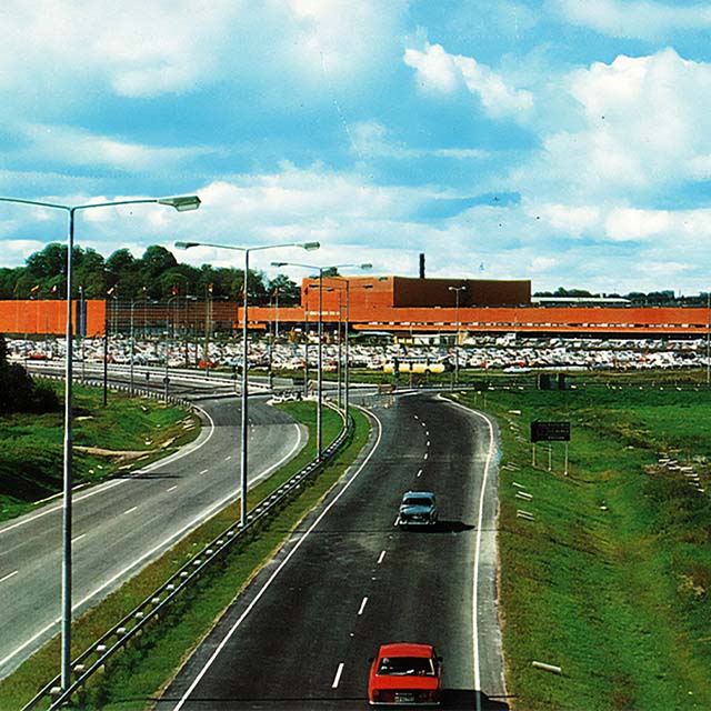 old photograph from the road and the junction of gamla huddingevägen and åbyvägen. in the background you can see the orange facade of the stockholm fair.