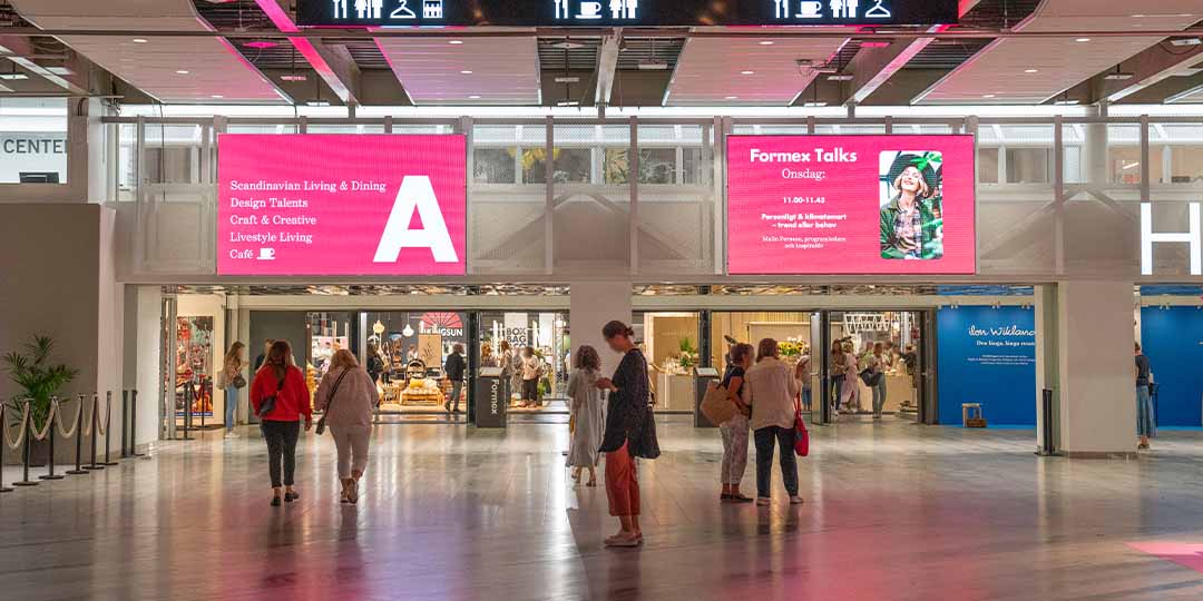 stora rosa digitala skärmar som leder in till hall A på Stockholmsmässan. Människor som rör sig framför skärmarna och är påväg in till en mässa