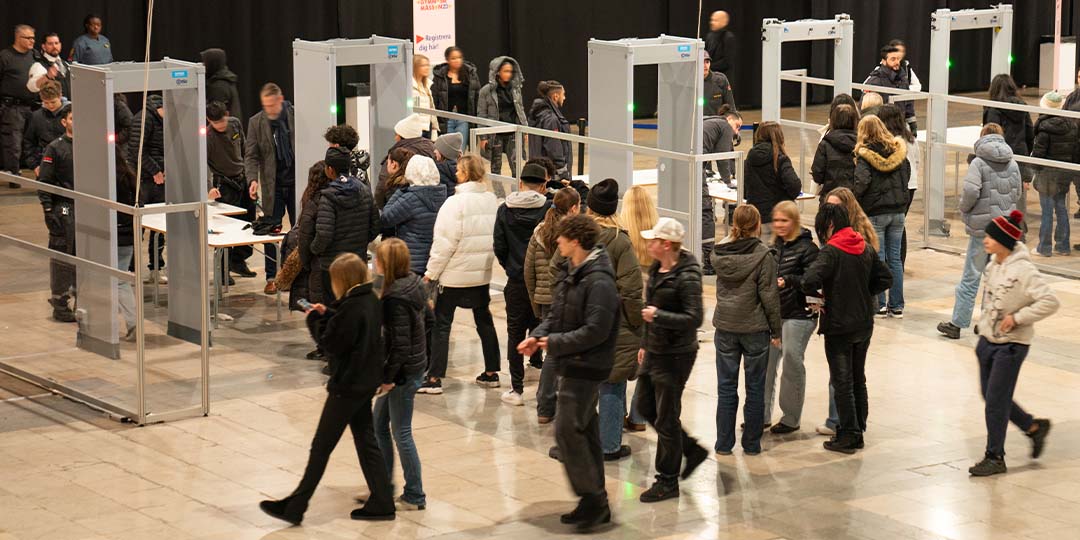Människor går igenom säkerhetskontroller vid en entré med metalldetektorer.